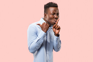 Image showing The young man whispering a secret behind her hand over pink background