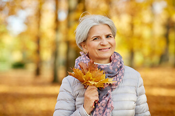 Image showing senior woman with maple leaves at autumn park