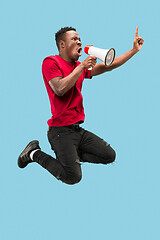 Image showing Soccer fan jumping on blue background. The young afro man as football fan with megaphone