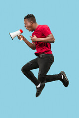 Image showing Soccer fan jumping on blue background. The young afro man as football fan with megaphone