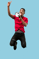 Image showing Soccer fan jumping on blue background. The young afro man as football fan with megaphone