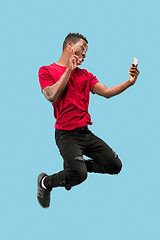 Image showing always on mobile. Full length of handsome young man taking phone while jumping