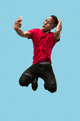 Image showing always on mobile. Full length of handsome young man taking phone while jumping