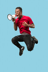 Image showing Soccer fan jumping on blue background. The young afro man as football fan with megaphone