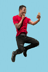 Image showing always on mobile. Full length of handsome young man taking phone while jumping