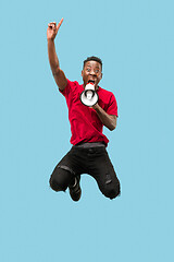 Image showing Soccer fan jumping on blue background. The young afro man as football fan with megaphone