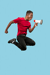 Image showing Soccer fan jumping on blue background. The young afro man as football fan with megaphone