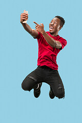 Image showing always on mobile. Full length of handsome young man taking phone while jumping