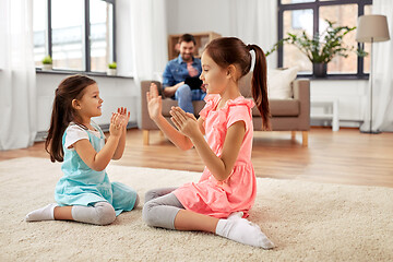 Image showing happy little sisters playing clapping game at home