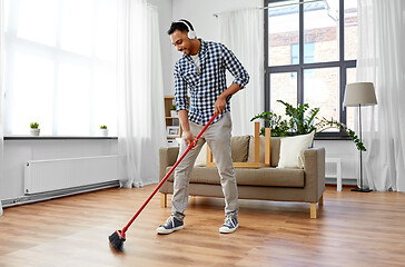 Image showing man in headphones with broom cleaning at home