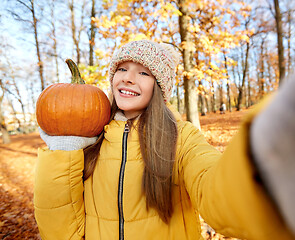 Image showing girl with pumpkin taking selfie at autumn park