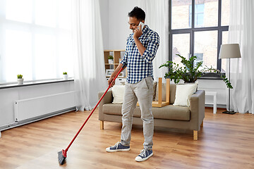 Image showing man with broom cleaning and calling on smartphone