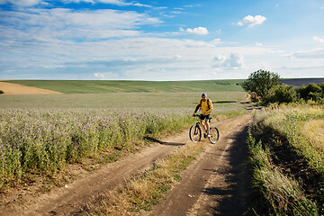 Image showing Cyclist riding a bike on off road to the sunset