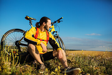 Image showing Cyclist resting on grass in mountains. Man is looking aside.