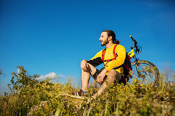 Image showing Cyclist resting on grass in mountains. Man is looking aside.