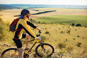 Image showing Cyclist riding a bike on off road to the sunset