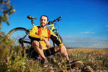 Image showing Cyclist resting on grass in mountains. Man is looking aside.