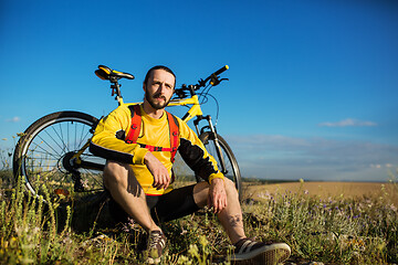 Image showing Cyclist resting on grass in mountains. Man is looking aside.