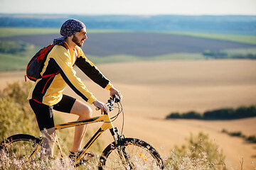 Image showing Cyclist riding a bike on off road to the sunset