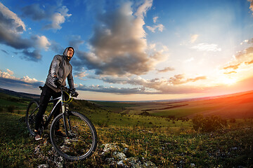 Image showing Young man cycling in a summer meadow at sunset
