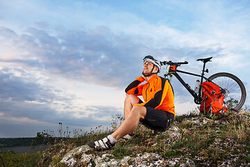 Image showing Cyclist resting on grass in mountains. Man is looking aside.