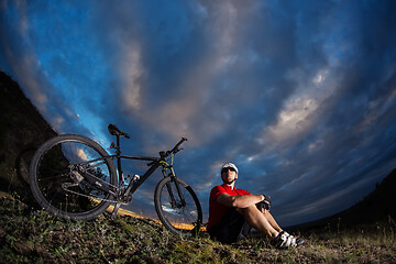 Image showing Cyclist resting on grass in mountains. Man is looking aside.