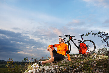 Image showing Cyclist resting on grass in mountains. Man is looking aside.