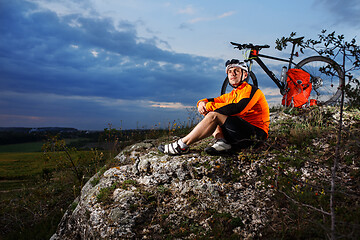 Image showing Cyclist resting on grass in mountains. Man is looking aside.