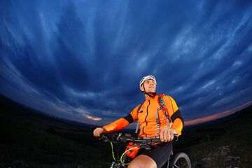 Image showing Man in helmet stay on bicycle under sky with clouds.