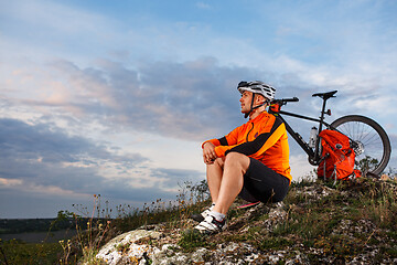 Image showing Cyclist resting on grass in mountains. Man is looking aside.