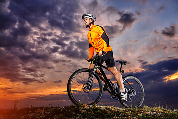 Image showing Man in helmet stay on bicycle under sky with clouds.