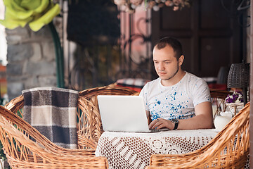 Image showing young man working on laptop at the wooden table outdoors