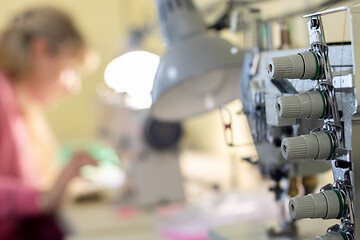 Image showing close-up of sewing equipment with threads and a worker in the background