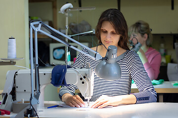 Image showing a seamstress works behind a sewing machine in a sewing shop at her workplace