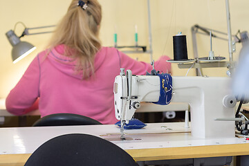 Image showing Girl sits with her back and sews on a sewing machine in a sewing shop