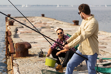 Image showing male friends with fishing rods on sea pier