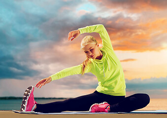 Image showing woman stretching on exercise mat at seaside