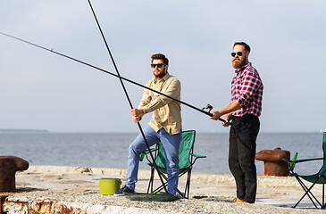 Image showing male friends with fishing rods on sea pier