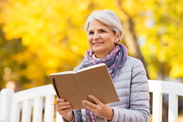 Image showing happy senior woman reading diary at autumn park