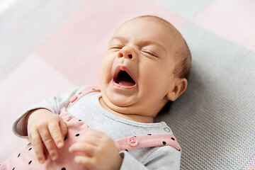 Image showing yawning baby girl in pink suit lying on blanket