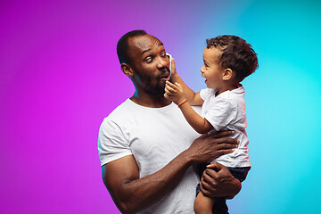 Image showing African-american father and son portrait on gradient studio background in neon