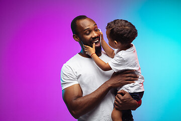 Image showing African-american father and son portrait on gradient studio background in neon