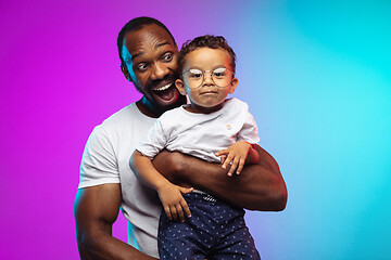 Image showing African-american father and son portrait on gradient studio background in neon