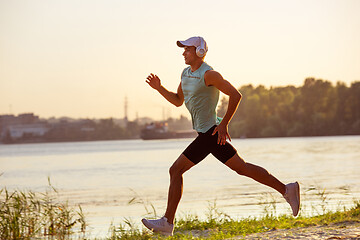 Image showing A young athletic man working out listening to the music at the riverside outdoors