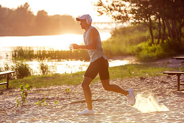 Image showing A young athletic man working out listening to the music at the riverside outdoors