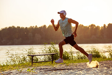 Image showing A young athletic man working out listening to the music at the riverside outdoors