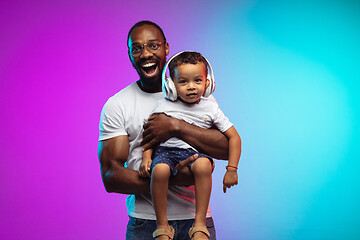 Image showing African-american father and son portrait on gradient studio background in neon