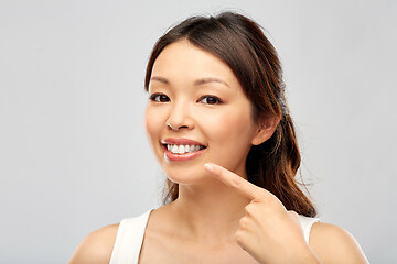 Image showing happy smiling young asian woman touching her face