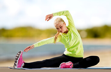 Image showing woman stretching on exercise mat on beach