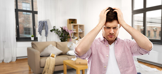 Image showing despaired young man in messy room having headache